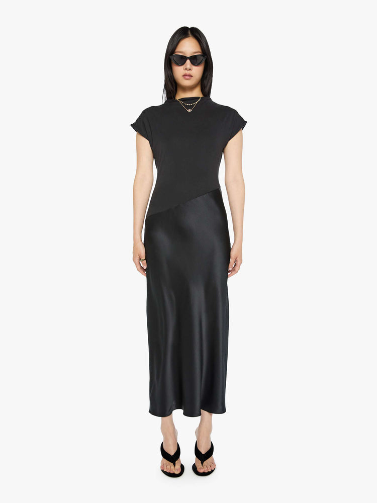 Front view of a woman in a black dress with a boat neck, short sleeves, a narrow fit and an ankle-length hem.