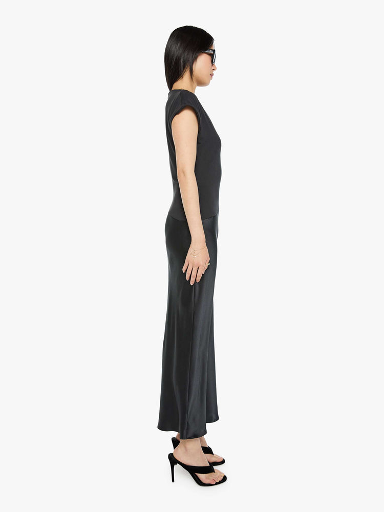 Side view of a woman in a black dress with a boat neck, short sleeves, a narrow fit and an ankle-length hem.