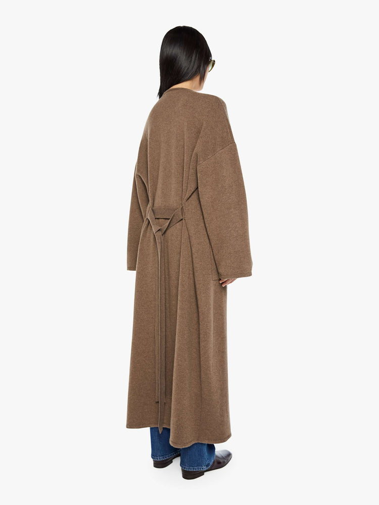 Back view of a woman in a chocolate brown trench coat with an oversized collar, drop shoulders, a tied waist and calf-length hem.