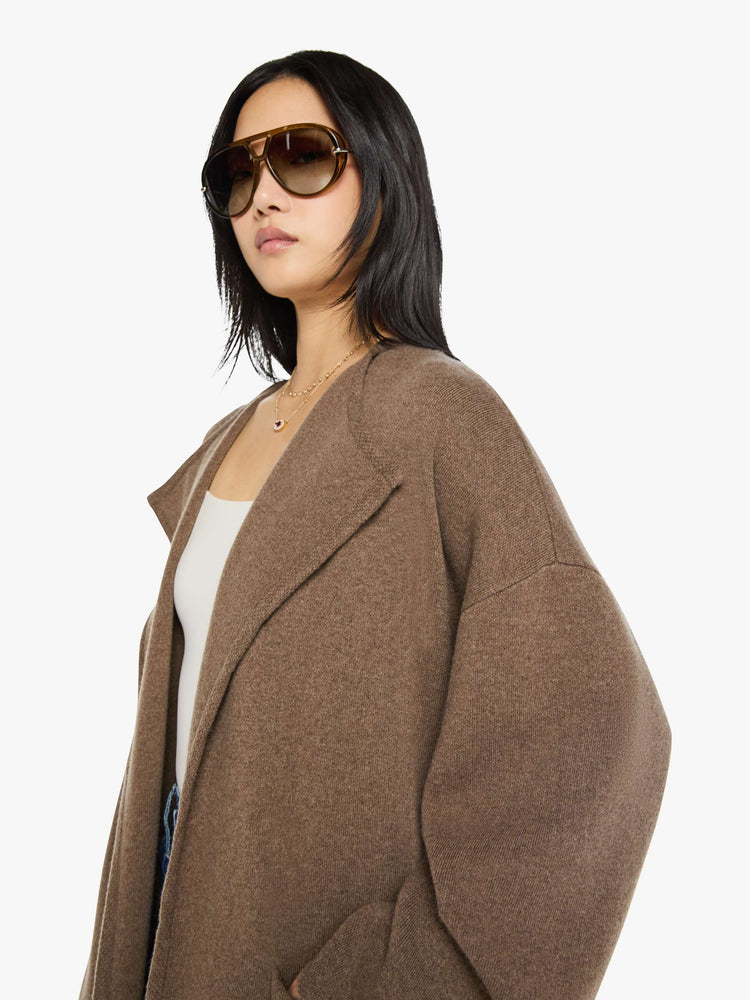 Close up view of a woman in a chocolate brown trench coat with an oversized collar, drop shoulders, a tied waist and calf-length hem.