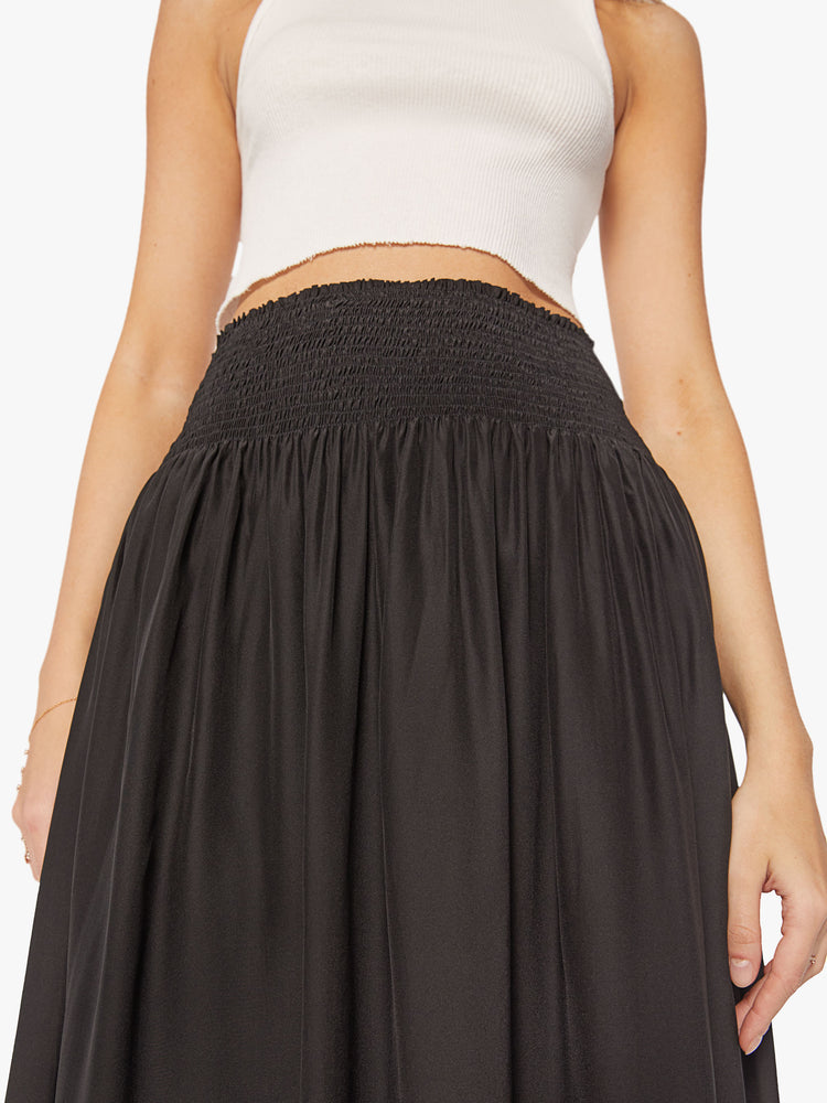 Front close up  view of a woman wearing a black skirt featuring a wide elastic waistband and a flowy fit, paired with a cropped white tank top.
