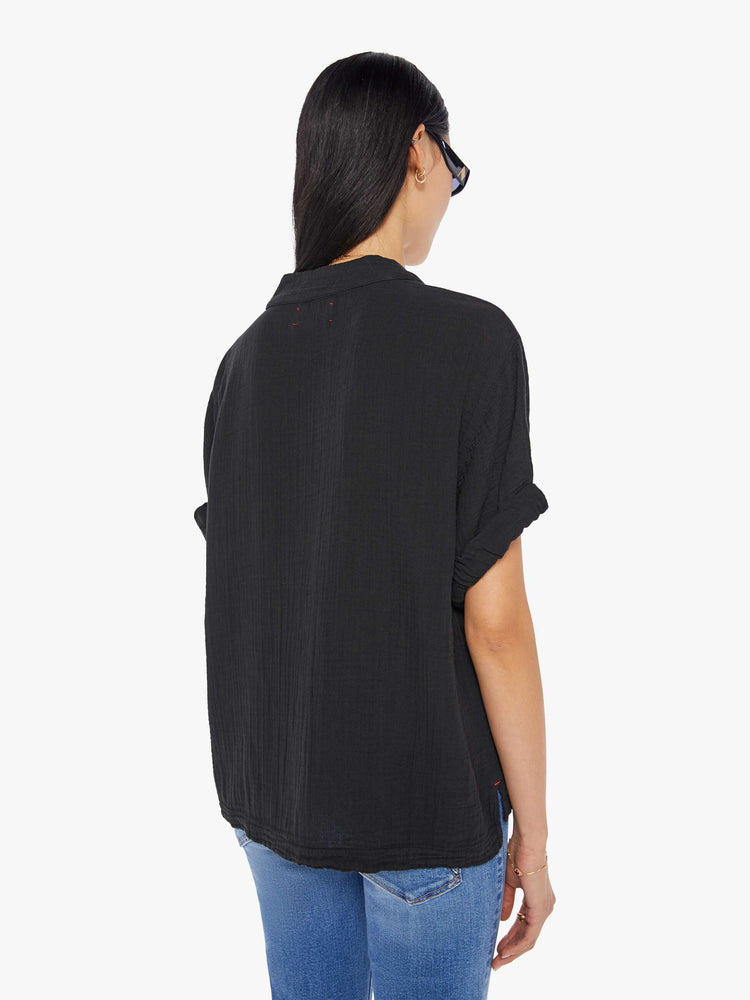 Back view of a woman wearing a black top featuring a deep v-neck, rolled sleeves, and a boxy fit.