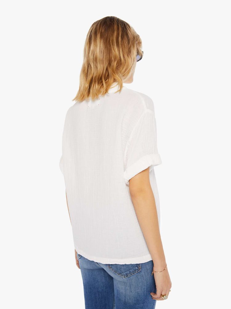 Back view of a woman wearing a white top featuring a deep v-neck, rolled sleeves, and a boxy fit.