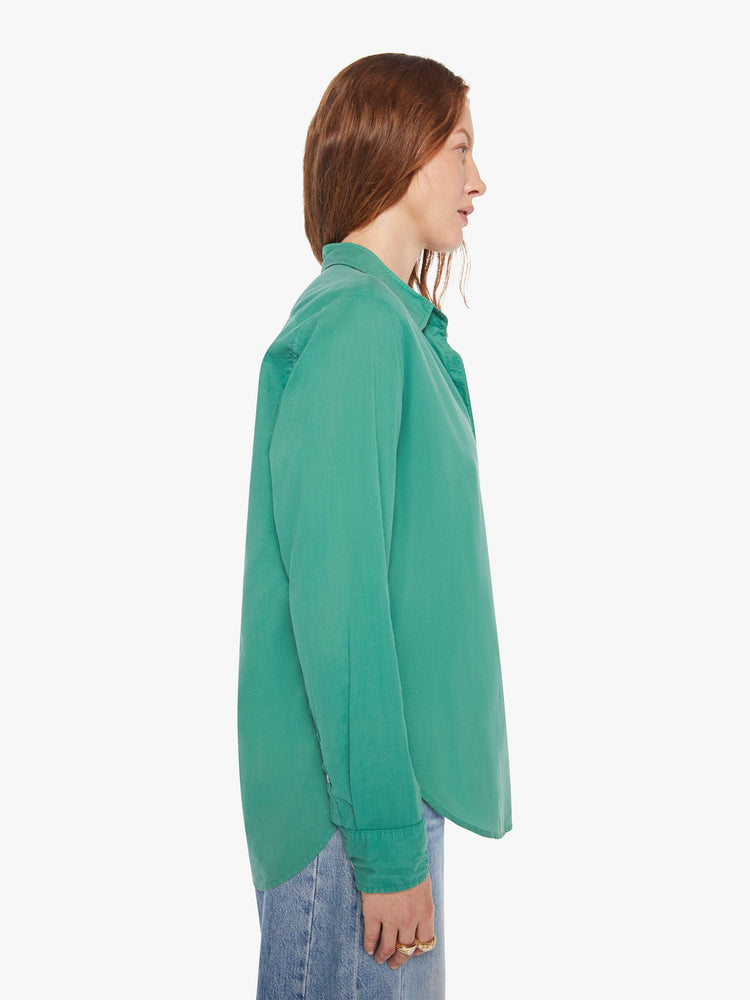 Side view of woman in a  green button-down long sleeve shirt.