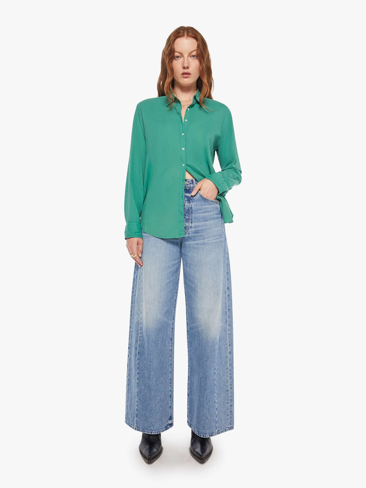 Full body view of woman in a  green button-down long sleeve shirt.