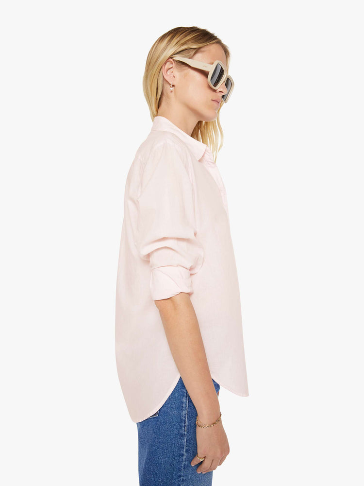 Side view of woman in a baby pink button-down long sleeve shirt.
