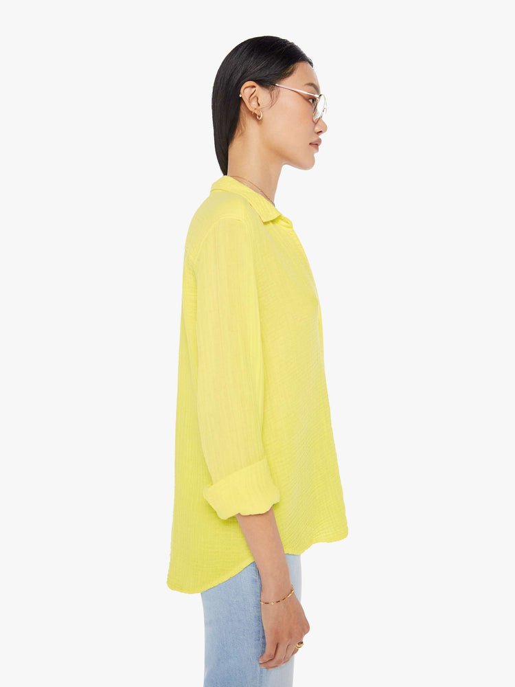 Side view of a womens bright yellow button down long sleeve shirt with a curved hem.