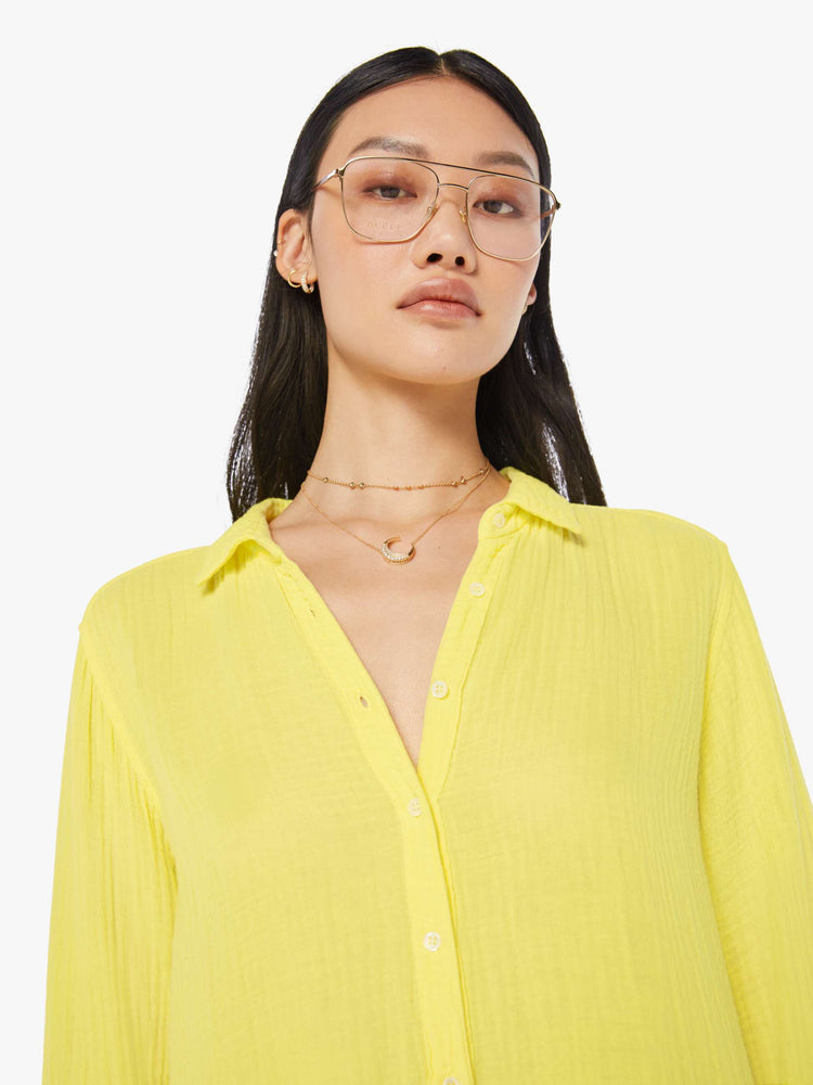 Front close up view of a womens bright yellow button down long sleeve shirt with a curved hem.