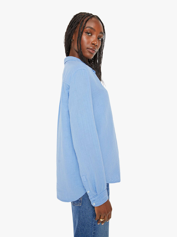 Side view of a woman blue button down long sleeve in a V-neck and curved hem with a light and airy fit.