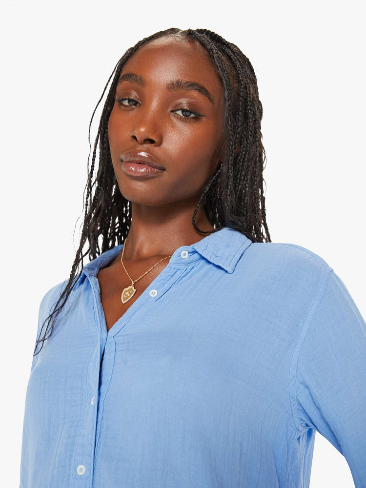 Close up view of a woman blue button down long sleeve in a V-neck and curved hem with a light and airy fit.