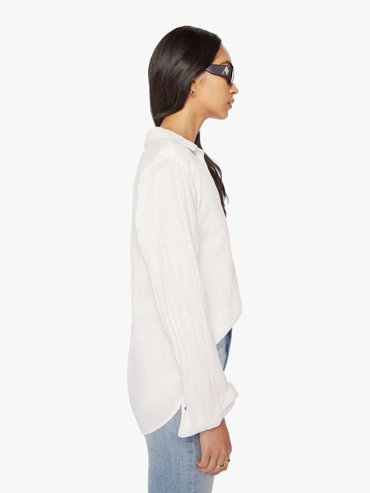 Side view of a woman white button-down features a V-neck and curved hem with a light and airy fit.