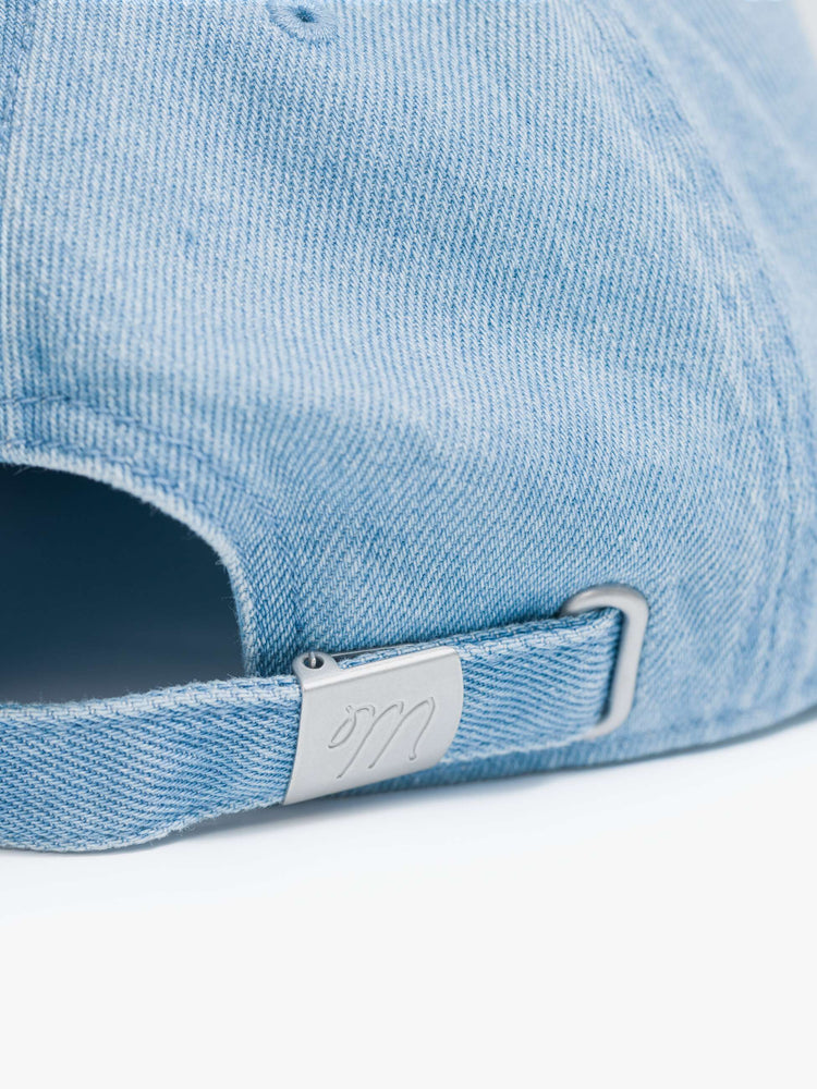 Close up view of a light denim hat with embroidered text in white and a bouquet of red flowers.