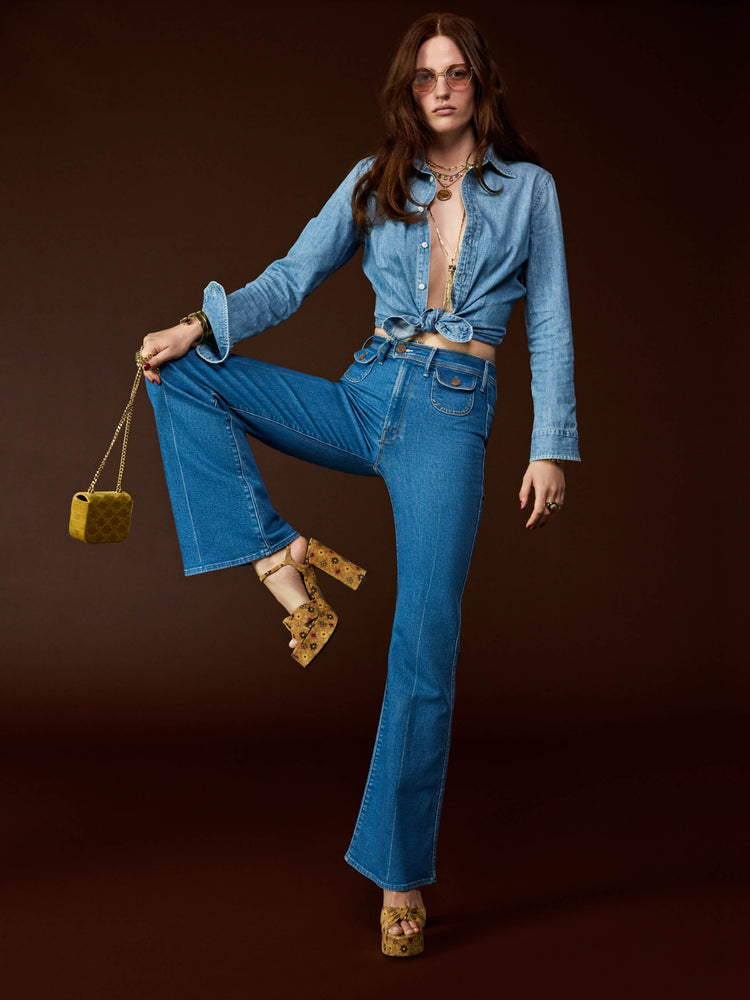 Styling view of a woman in a mid blue wide leg jean features a high rise, buttoned waistband, zip fly, small patch pockets, long 32-inch inseam and a clean hem.