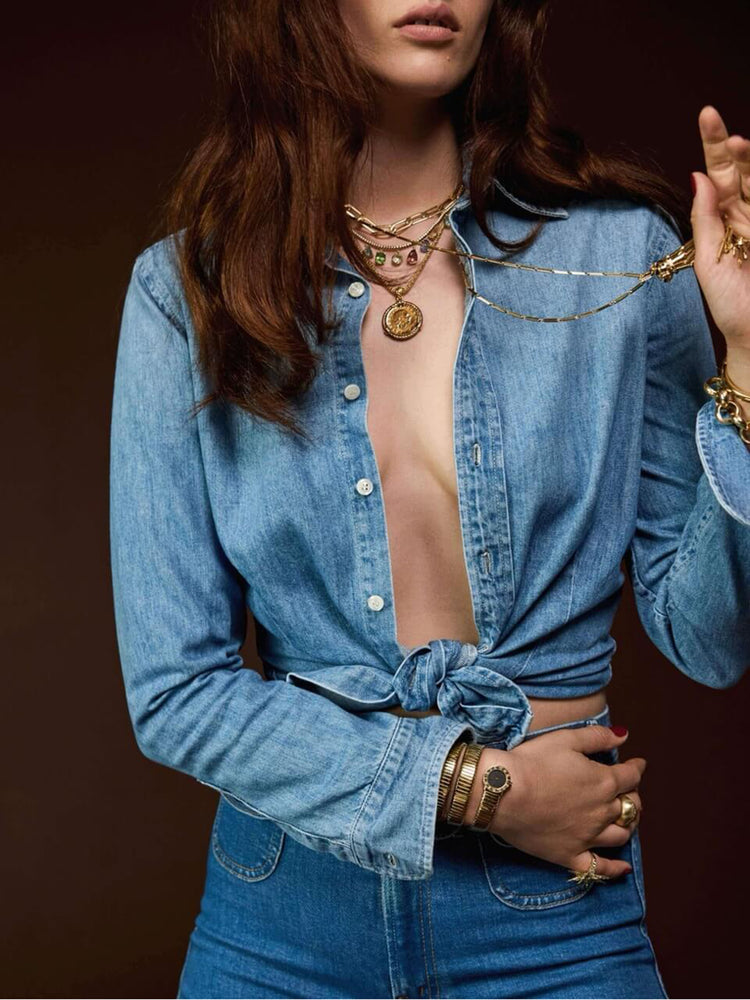Styling view of a woman in a light blue denim button-up features curved hems and seamed details for a more narrow fit.