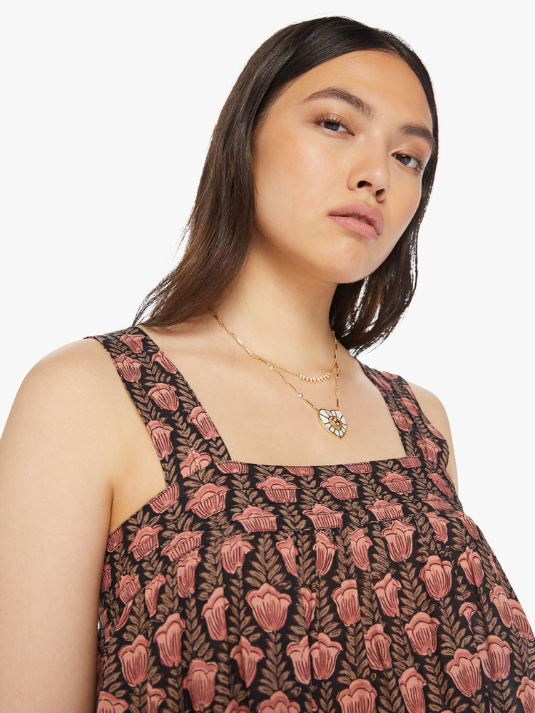 Close up view of a woman top designed in brown with a baby pink tulip print, and features detailed straps and buttons in the back.