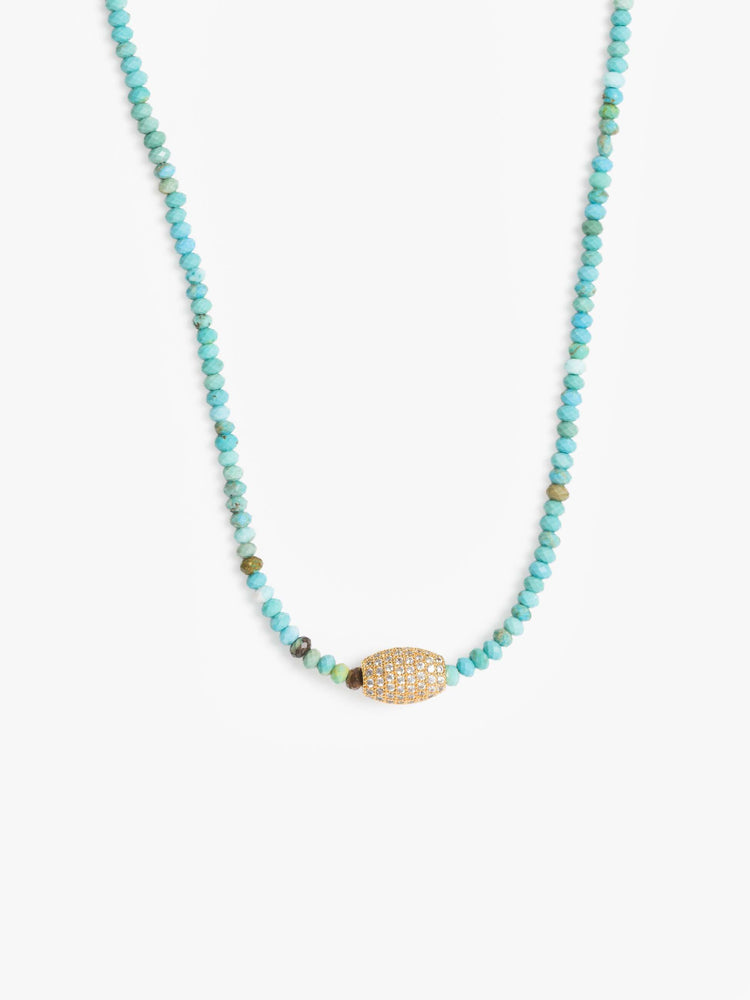 Close up view of a beaded necklace with turquoise and gold beads and a gold-plated oval charm.