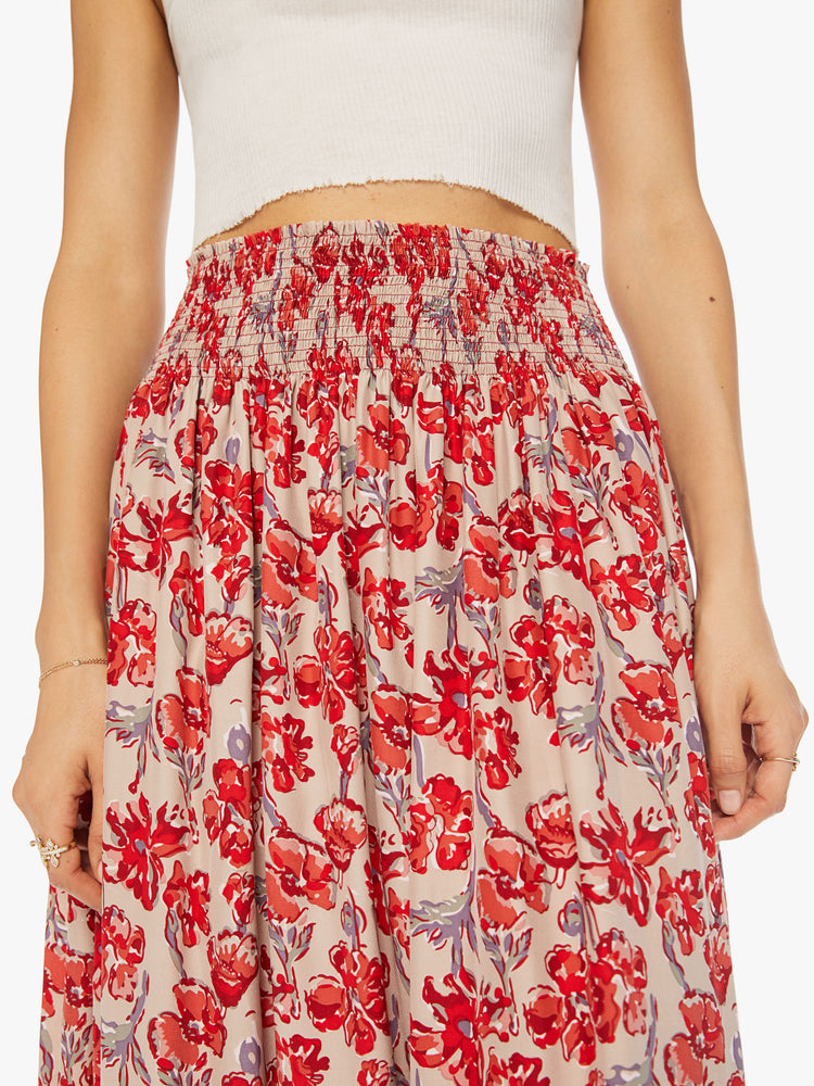 Close up view of a woman in a nude with red watercolor floral print maxi skirt with a smocked waistband and a loose, flowy fit.