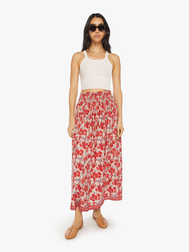 Front view of a woman in a nude with red watercolor floral print maxi skirt with a smocked waistband and a loose, flowy fit.