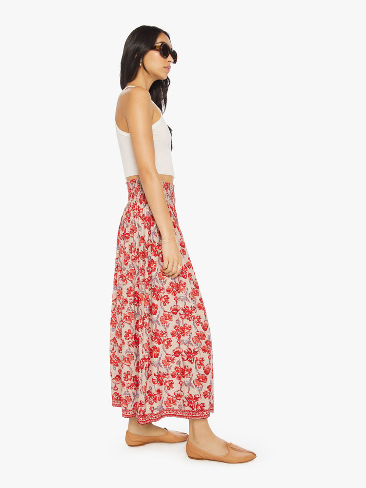 Side view of a woman in a nude with red watercolor floral print maxi skirt with a smocked waistband and a loose, flowy fit.