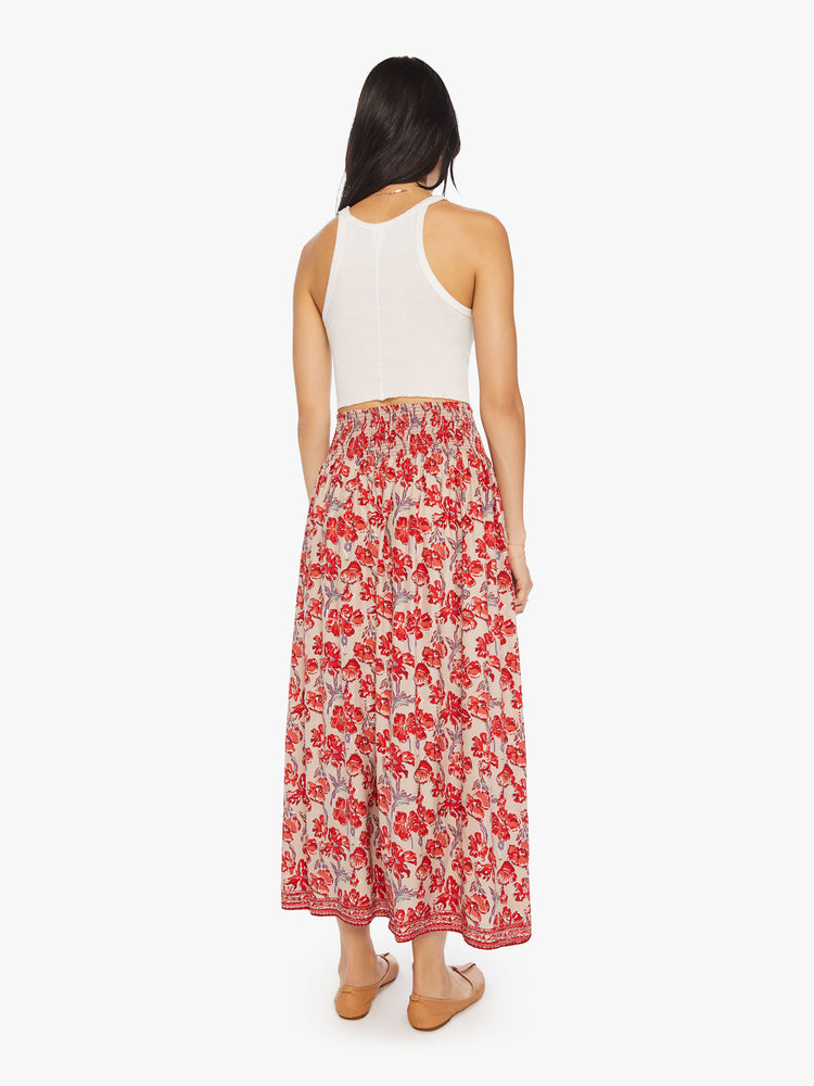 Back view of a woman in a nude with red watercolor floral print maxi skirt with a smocked waistband and a loose, flowy fit.