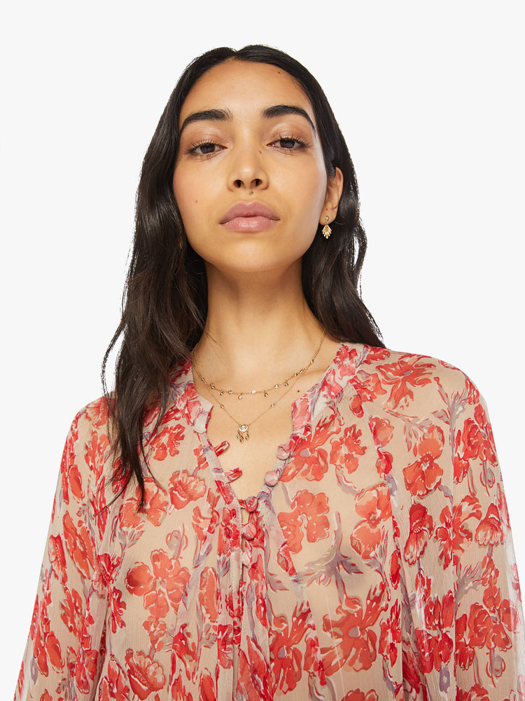 Close up view of a woman sheer nude and red watercolor floral print maxi dress with designed with voluminous sleeves and has an A-line cut.