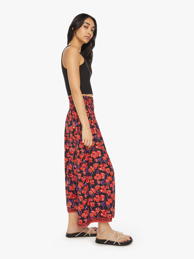 Side view of a woman black/red watercolor floral print with a smocked waistband and a loose, flowy fit.