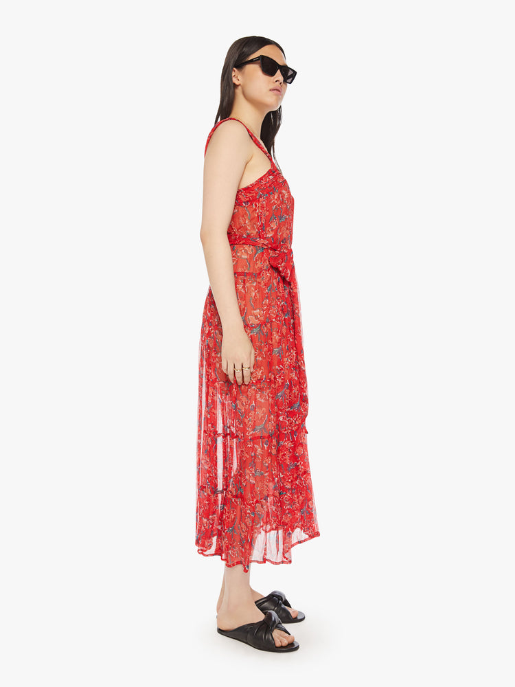 Side view of a woman red maxi dress with colorful print with a square neck, detailed straps, optional waist sash and an ankle-grazing hem.