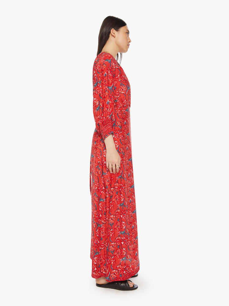 Side view of a woman in a red dress with a colorful floral print, and features a V-neck, tied waist and long maxi skirt with a loose, flowy fit.