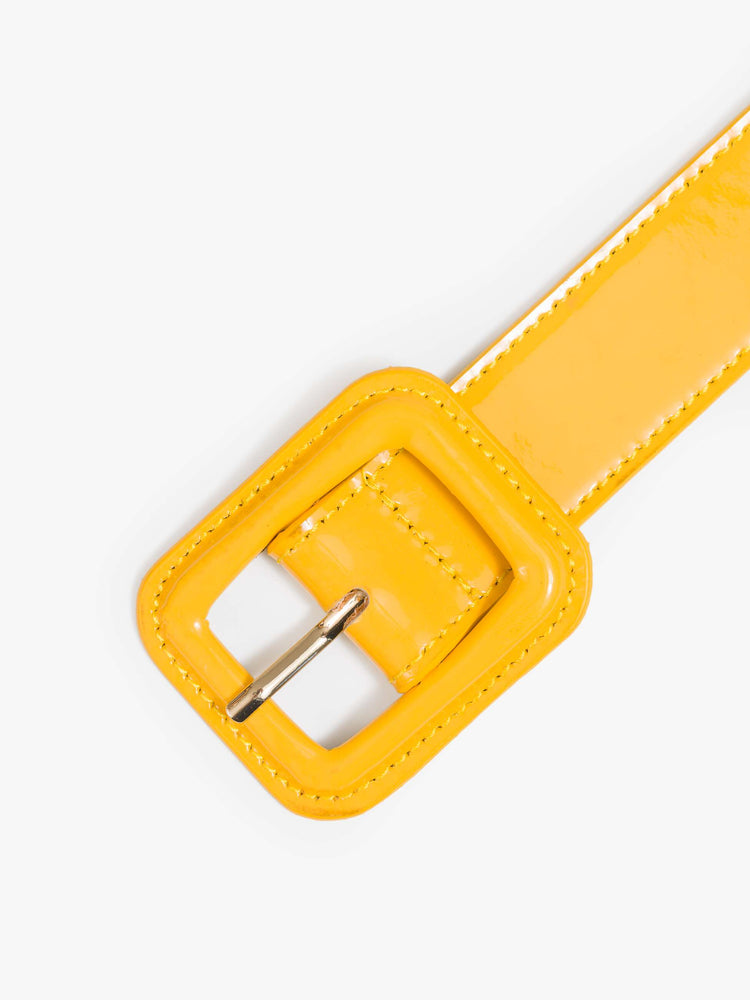 Close up view of a yellow patent leather belt with an oversized square buckle. 