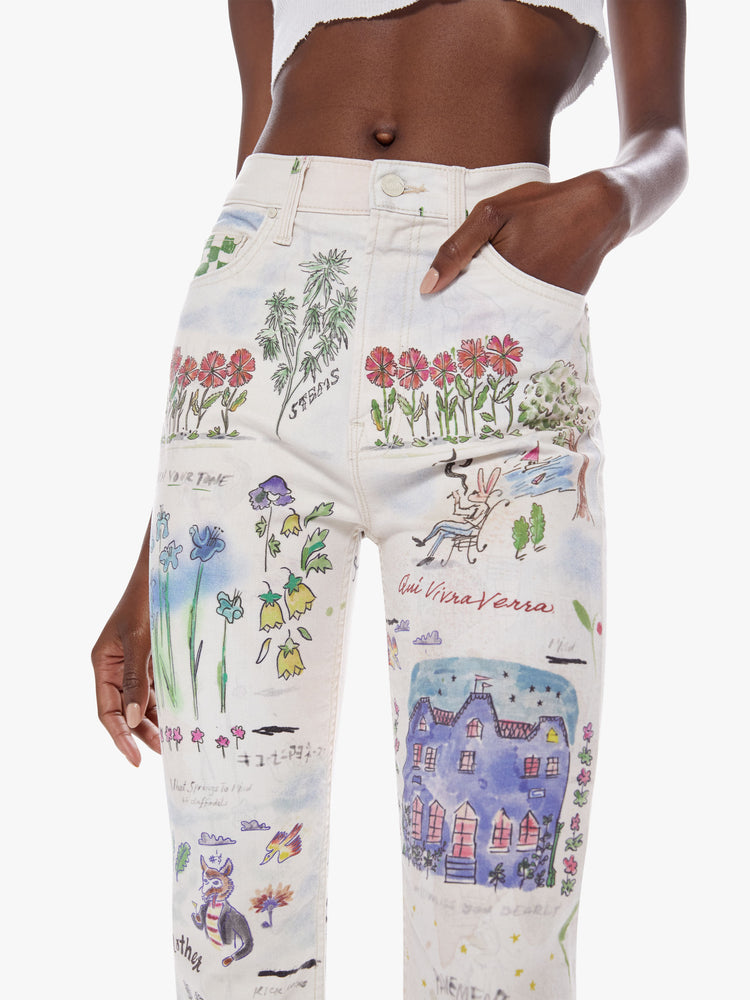 Close up waist view of a woman high-waisted straight leg has a 31-inch inseam and a clean hem in an off-white hue with colorful, storybook-inspired graphic illustrations.