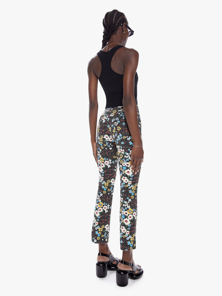 Back full body view of a woman in a high rise flare with a narrow leg, ankle length inseam, and a clean hem made from cotton with a touch of stretch, pushing daises is a high contrast floral print in black, blue, yellow, red, and white