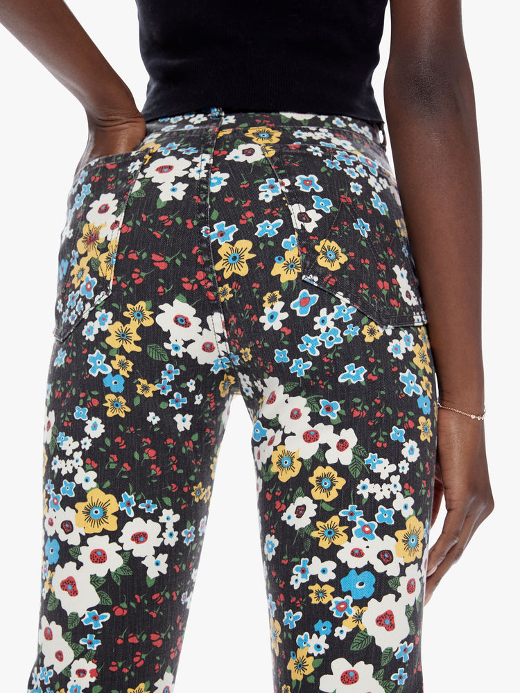 Close up back view of a woman in a high rise flare with a narrow leg, ankle length inseam, and a clean hem made from cotton with a touch of stretch, pushing daises is a high contrast floral print in black, blue, yellow, red, and white