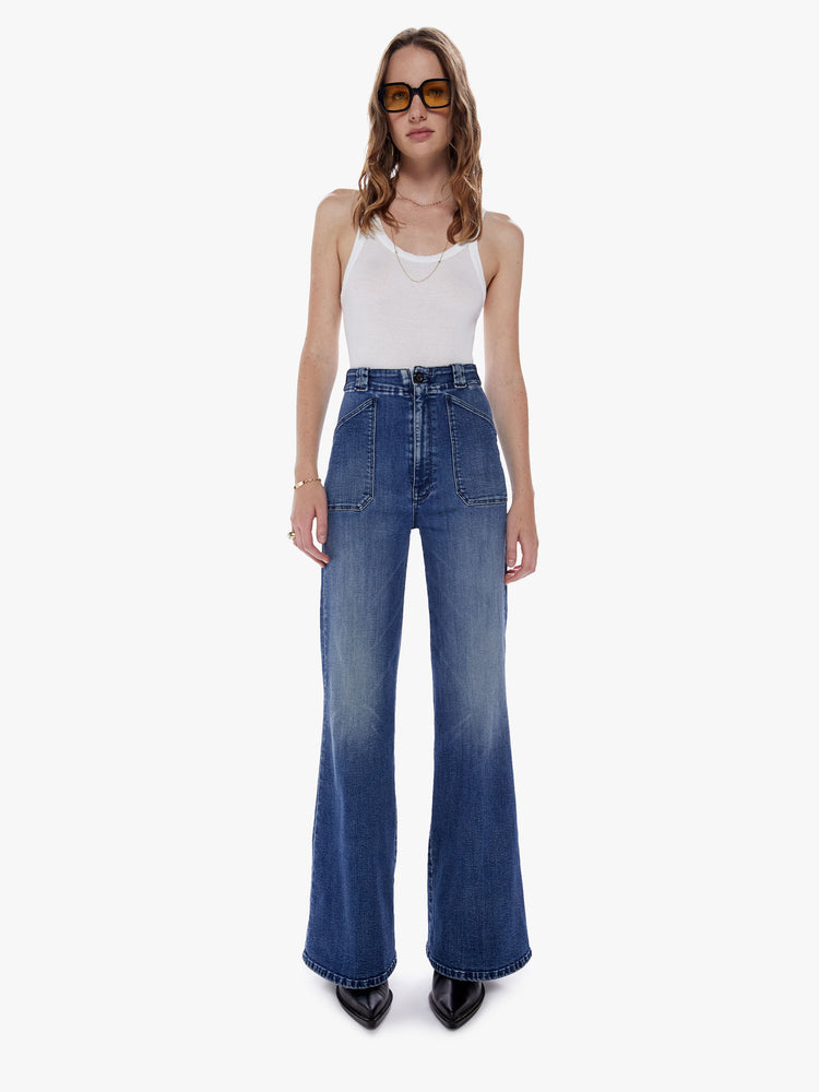 Front full body view of a woman in an inspired wide leg pant with a high rise, patch pockets, long 32 inch inseam, and loose fit made from denim with a touch of stretch in a dark blue wash with subtle fading and whiskering
