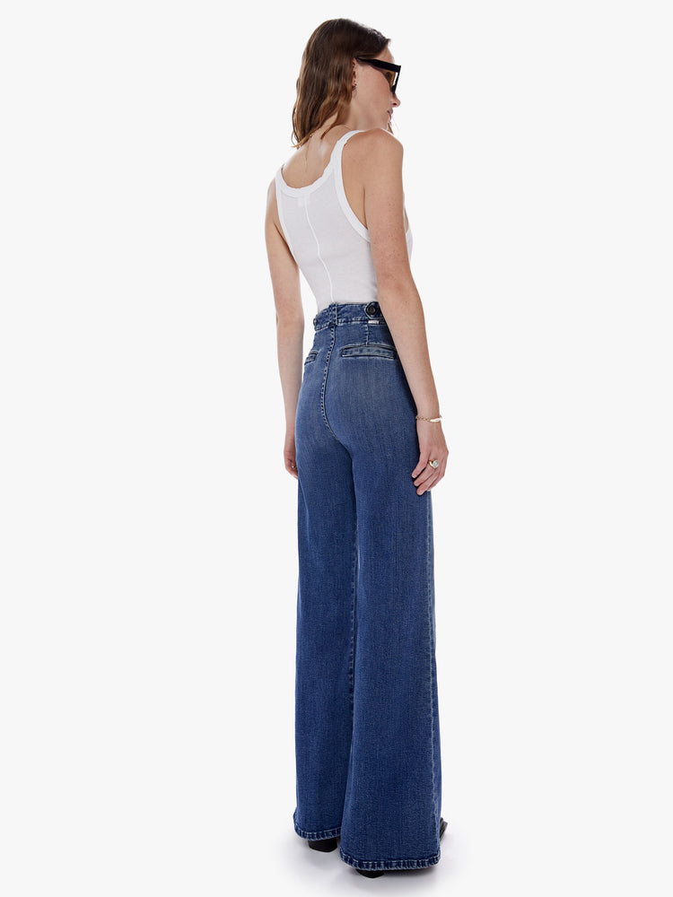 Back full body view of a woman in an inspired wide leg pant with a high rise, patch pockets, long 32 inch inseam, and loose fit made from denim with a touch of stretch in a dark blue wash with subtle fading and whiskering