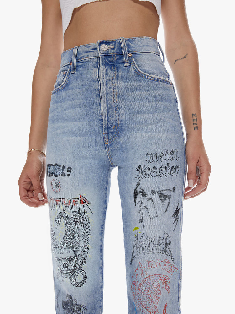 Waist close view of a woman in an ultra high waisted straight leg with a button fly and a clean ankle length inseam cut from semi rigid superior denim in a light blue wash with whiskering, fading and angsty graphic doodles down the legs