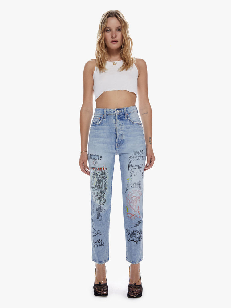 Front view of a woman in an ultra high waisted straight leg with a button fly and a clean ankle length inseam cut from semi rigid superior denim in a light blue wash with whiskering, fading and angsty graphic doodles down the legs.