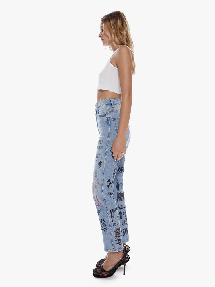 Side view of a woman in an ultra high waisted straight leg with a button fly and a clean ankle length inseam cut from semi rigid superior denim in a light blue wash with whiskering, fading and angsty graphic doodles down the legs