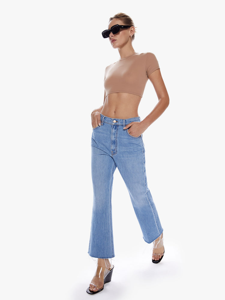 In motion full body view of a woman in a flare jean from SNACKS mothers homage to throwback styles of the 80s and 90s designed to be worn loose and low at the hips, the jeans feature a relaxed fit, slightly dropped crotch and frayed ankle inseam in a mid blue wash