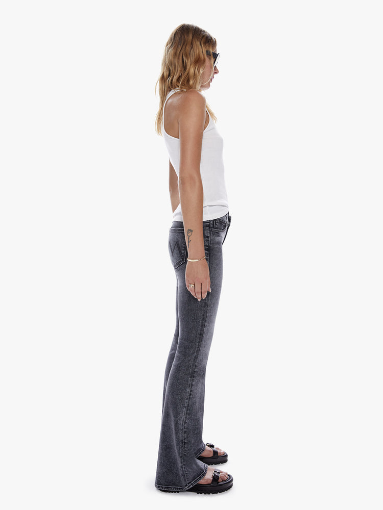 Side view of a woman in a super low rise flare with a long 34 inch inseam and a clean hem cut from soft stretch denim, in a black mineral wash with a high contrast fading throughout