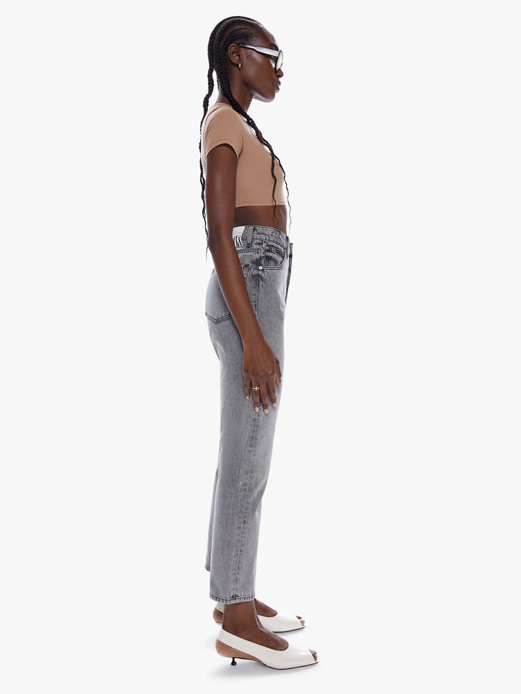 Side full body view of a woman in straight leg jean from snacks mothers homage to throwback styles of the 80s and 90s, the super high waisted jean feature a narrow straight leg with a clean ankle length inseam in a washed grey hue