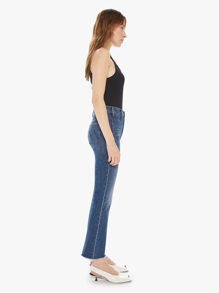 Side view of a women's medium blue high rise flare with patch pockets and a frayed ankle length inseam