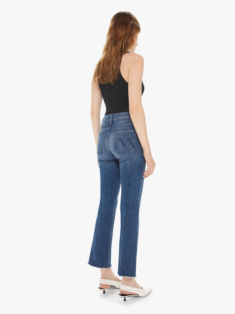 Back view of a women's medium blue high rise flare with patch pockets and a frayed ankle length inseam
