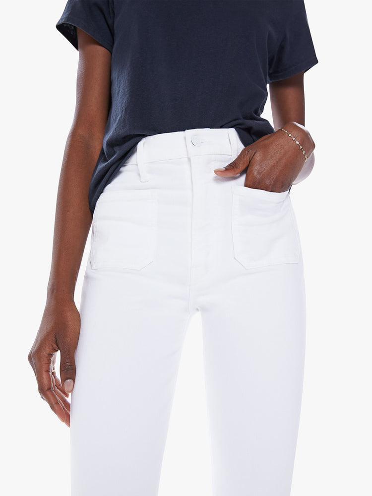 Close up waist view of a woman's high-rise flare jeans with patch pockets and a frayed ankle-length inseam in white denim.