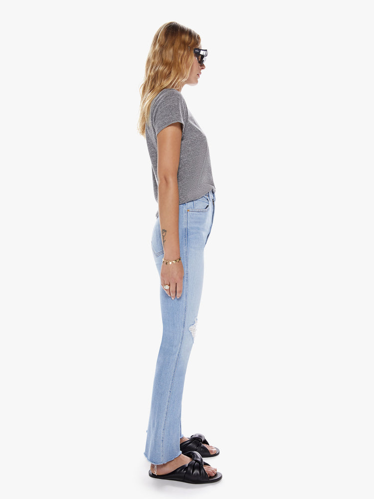 Side view of a womens light blue wash jean with a high rise, frayed hem and distressed knees.