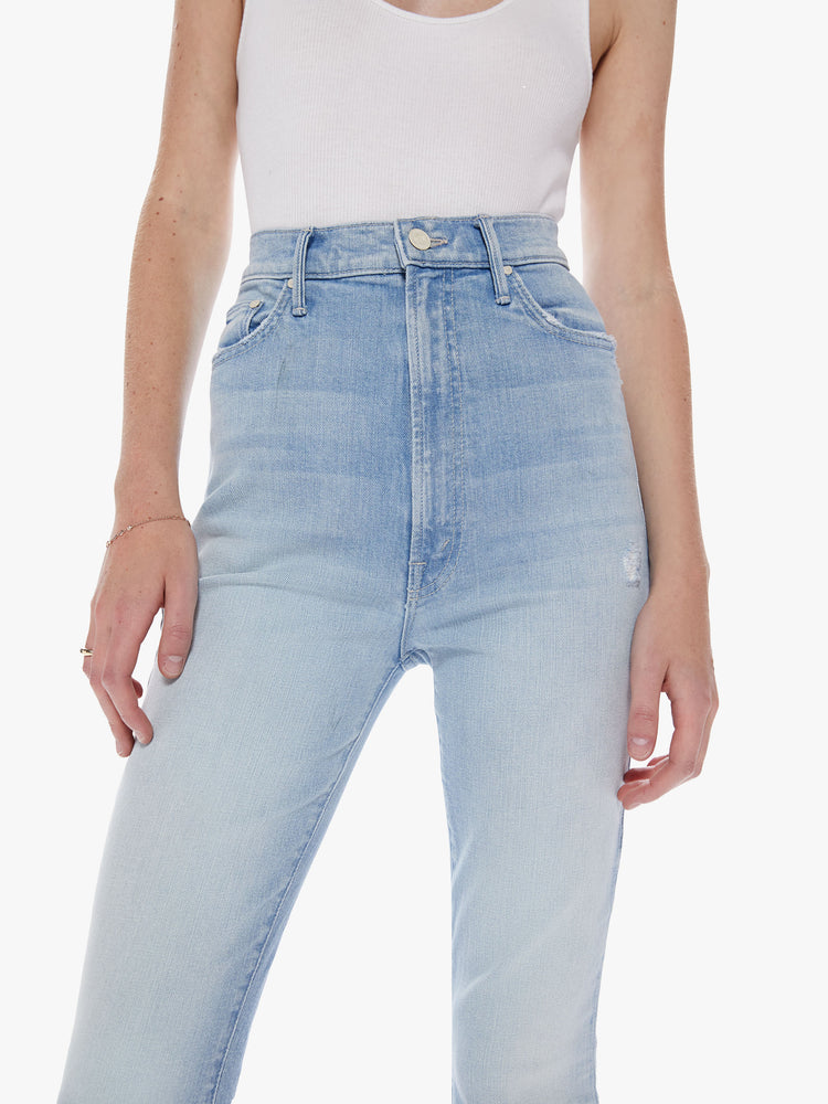 Waist close  up view of woman super high-waisted bootcut has an ankle-length inseam and a frayed hem in a light blue wash.