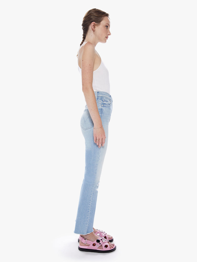Side view of woman super high-waisted bootcut has an ankle-length inseam and a frayed hem in a light blue wash.