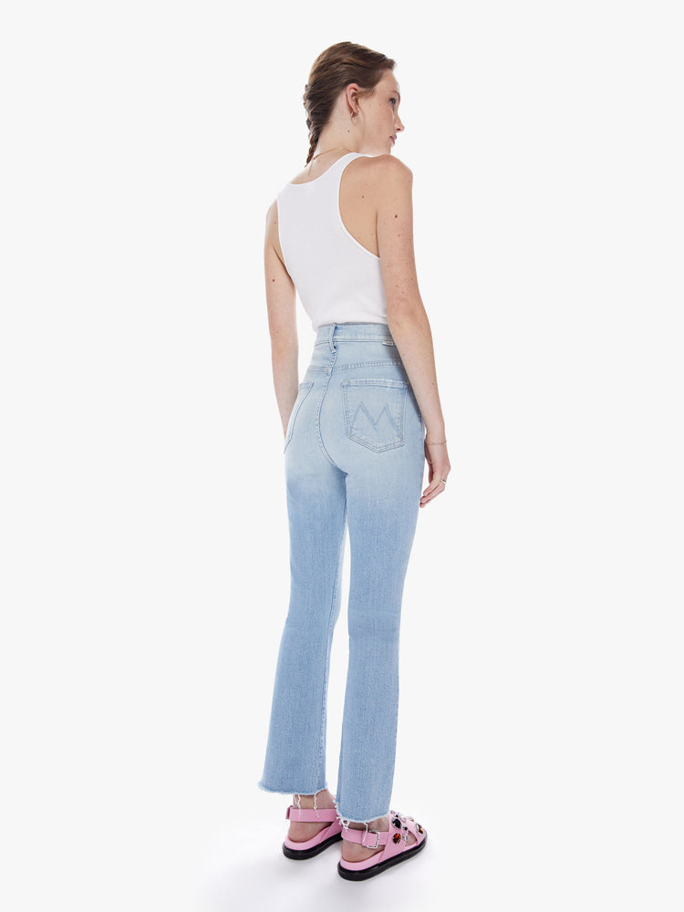 Back view of woman super high-waisted bootcut has an ankle-length inseam and a frayed hem in a light blue wash.
