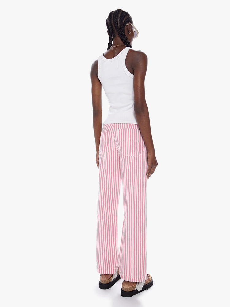Back view of a woman High-waisted wide-leg pants with buttons at the hips, a hammer loop, a cargo pocket and low-set back pockets in a pink railroad stripe pattern with white buttons.