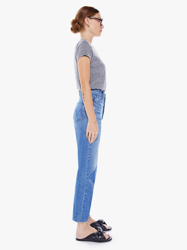 Side view of woman Ultra high-rise jeans with a straight, narrow leg and a cropped inseam in mid-blue wash with dark patches at the knees.