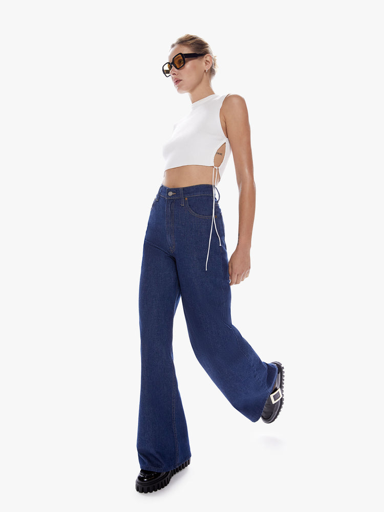 Front in motion full body view of a woman in Snacks widest leg jean from mothers homage to throwback styles of the 80s and 90s, the high rise jeans feature a loose, super full leg and a long 32-inch inseam in a dark blue wash